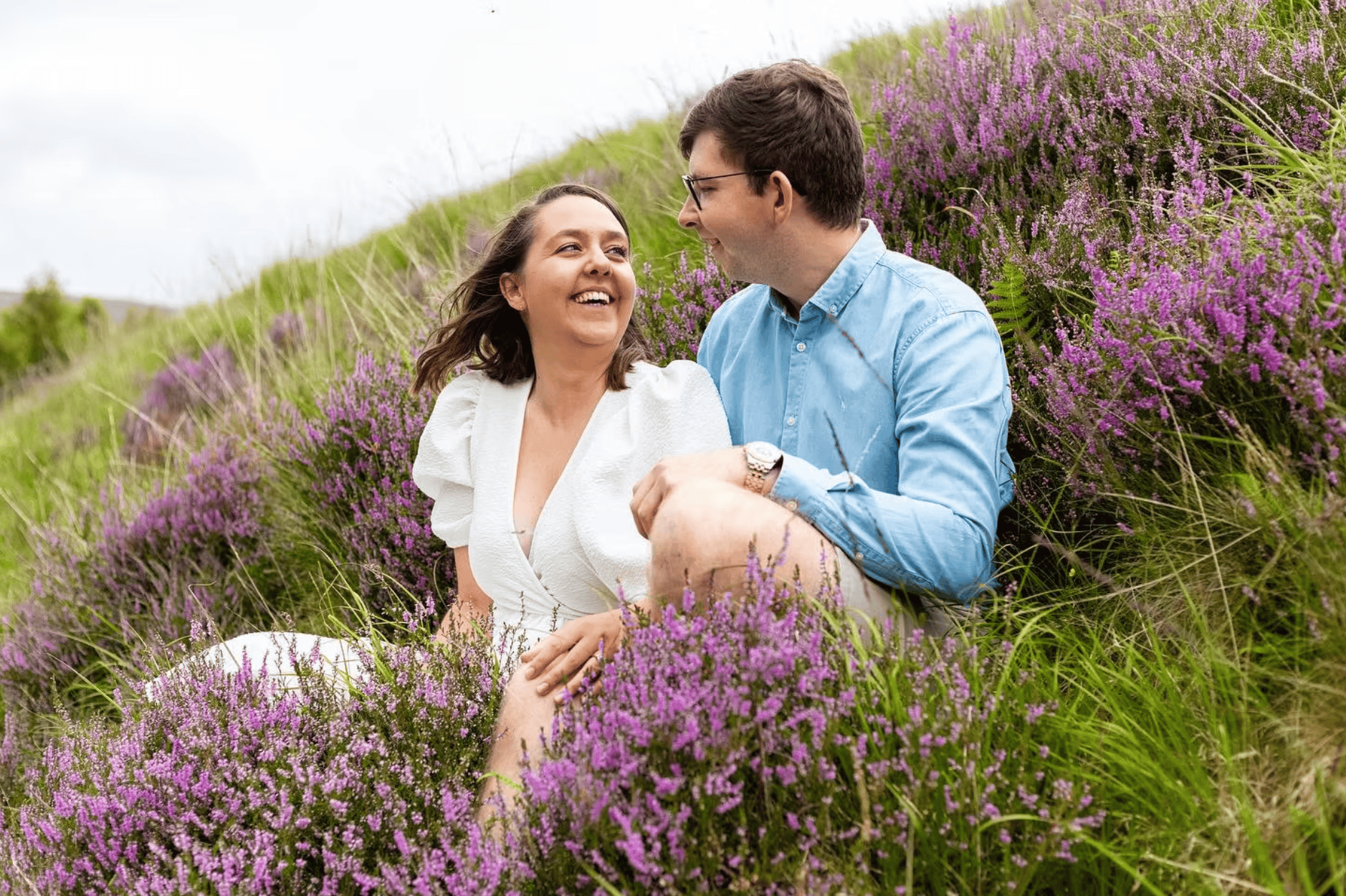 Couple sitting together laughing in purple Scottish heather on a hillside